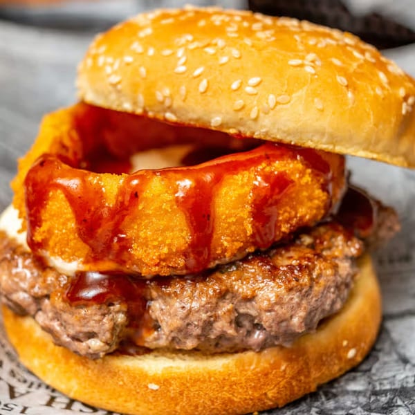 Close-up of a Gleasons Bar burger with a thick patty, onion ring, and barbecue sauce.