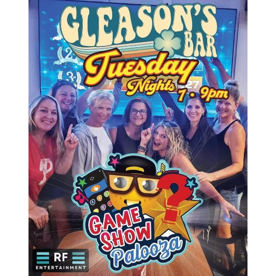 Seven smiling women pose in front of a Gleasons Bar sign advertising "Tuesday Nights Game Show Palooza".