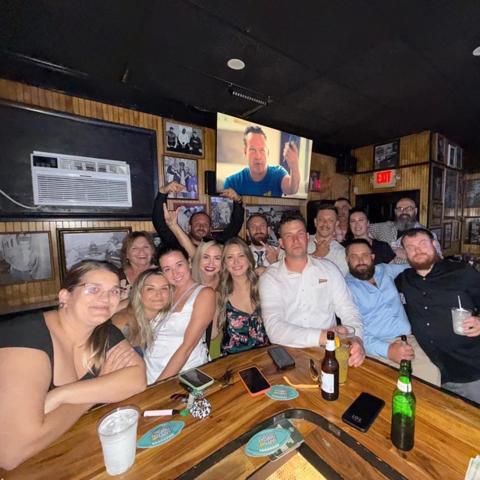 A large group of friends smiling and posing for a photo at a wooden bar inside Gleason's Bar.