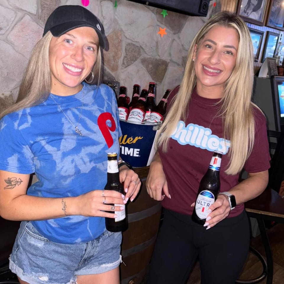 Two smiling women holding beer bottles, standing next to a bucket of Budweiser at Gleasons Bar.