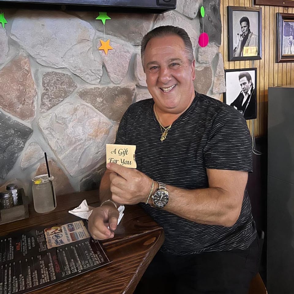 A smiling man in a striped shirt holds a "A Gift For You" card at Gleasons Bar.