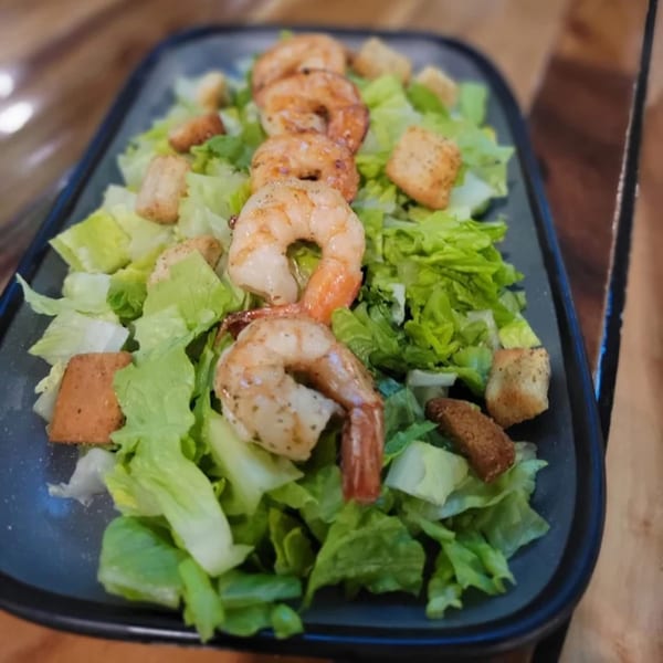 A long black plate of fresh green lettuce, croutons, and five grilled shrimp.