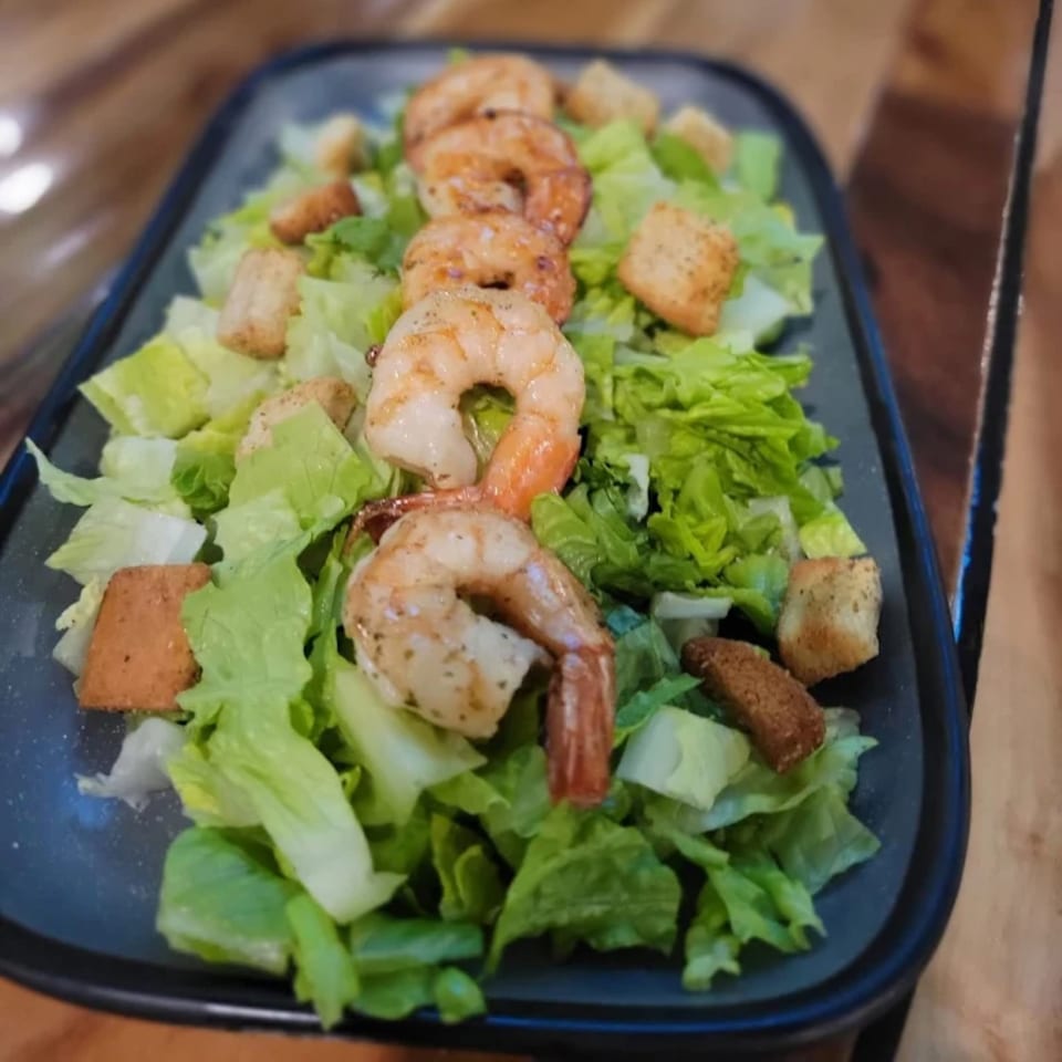 A long black plate of fresh green lettuce, croutons, and five grilled shrimp.