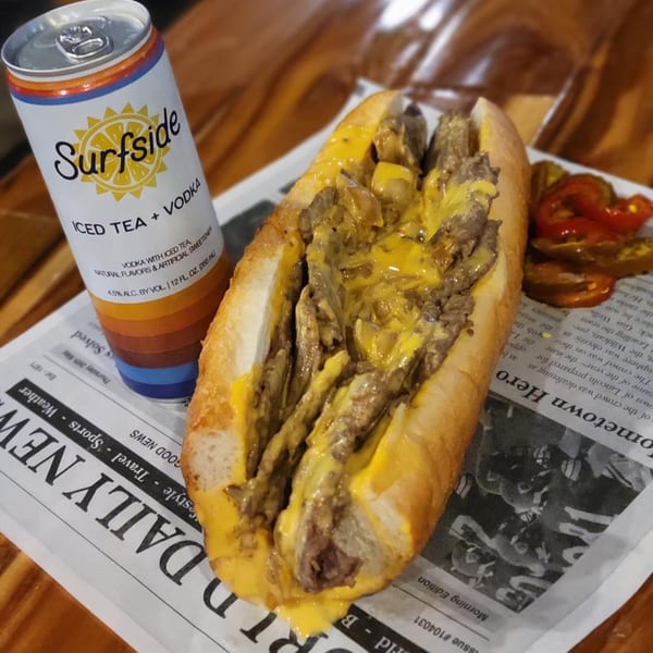 A Gleasons Bar cheesesteak with melted cheese and a Surfside iced tea can on a newspaper.
